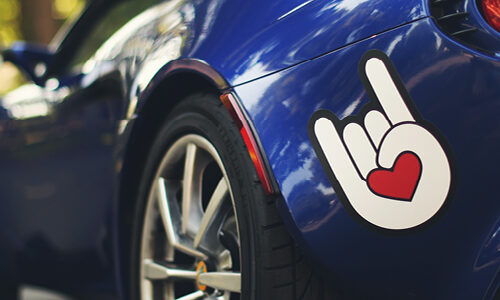 bold love heart/hand stick on the bumper o fa blue sports car - image by Sticker Mule via unsplash.com